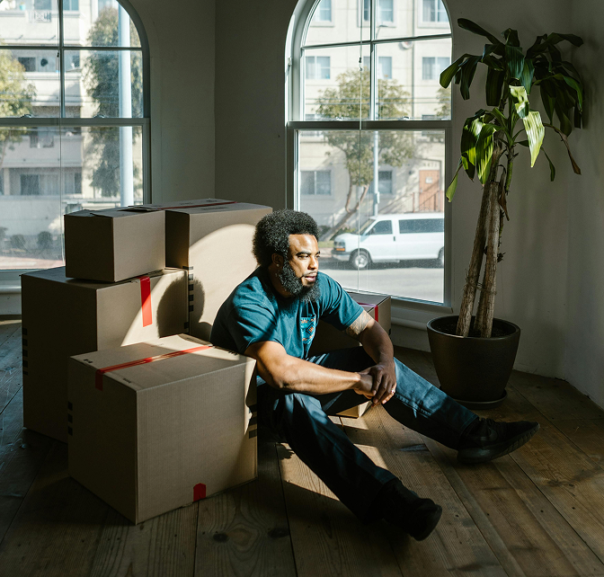 Man sitting down on the floor in his home surrounded by moving boxes